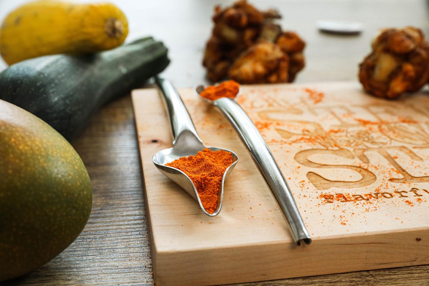 Chef Stew's Signature Seasoning Blend on measuring spoons with fresh produce and chicken lollipops in background